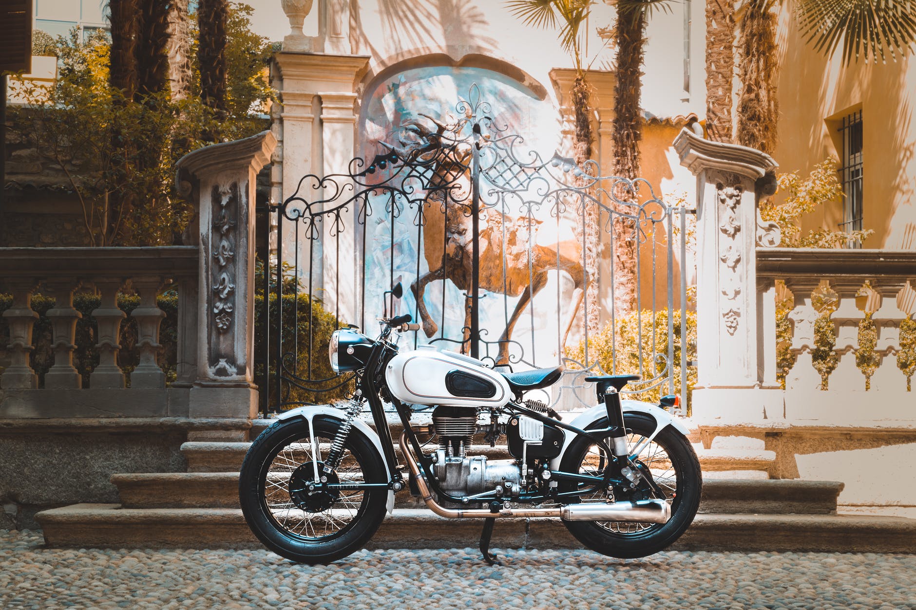 white cafe racer motorcycle parked next to an iron gate